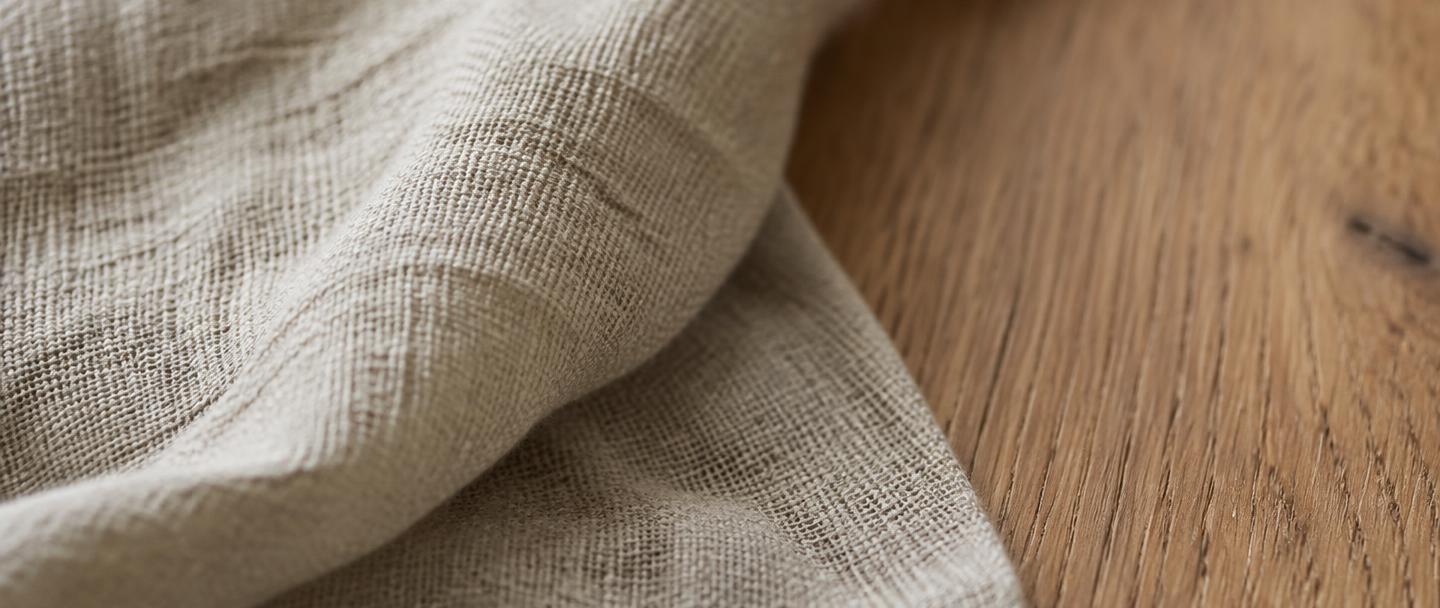 Raw undyed linen resting on solid oak, shown close up
